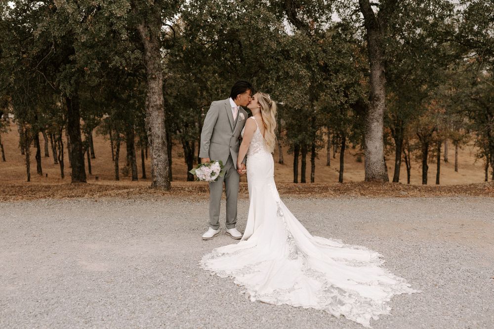 A couple in wedding attire poses together in a wooded outdoor setting during their special day.