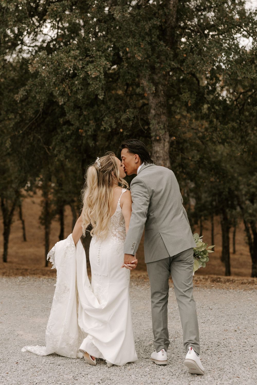 A couple shares a romantic kiss outdoors in a natural setting with trees in the background.