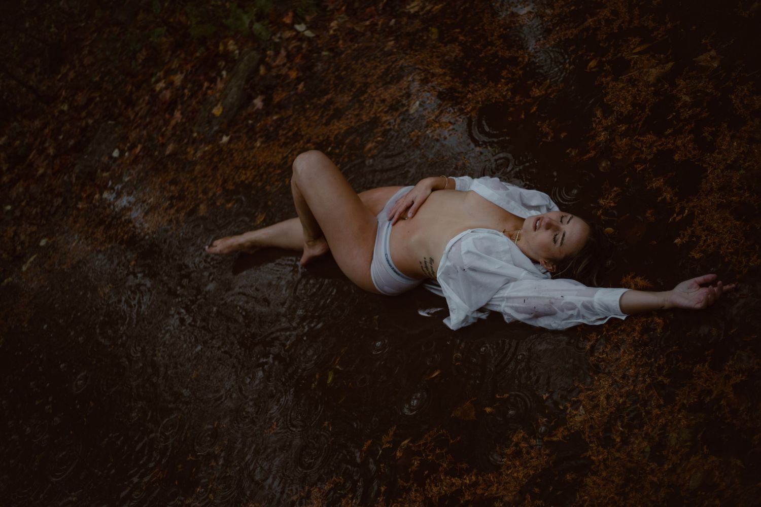 Model lies in a puddle for her self love portrait session in the rain.