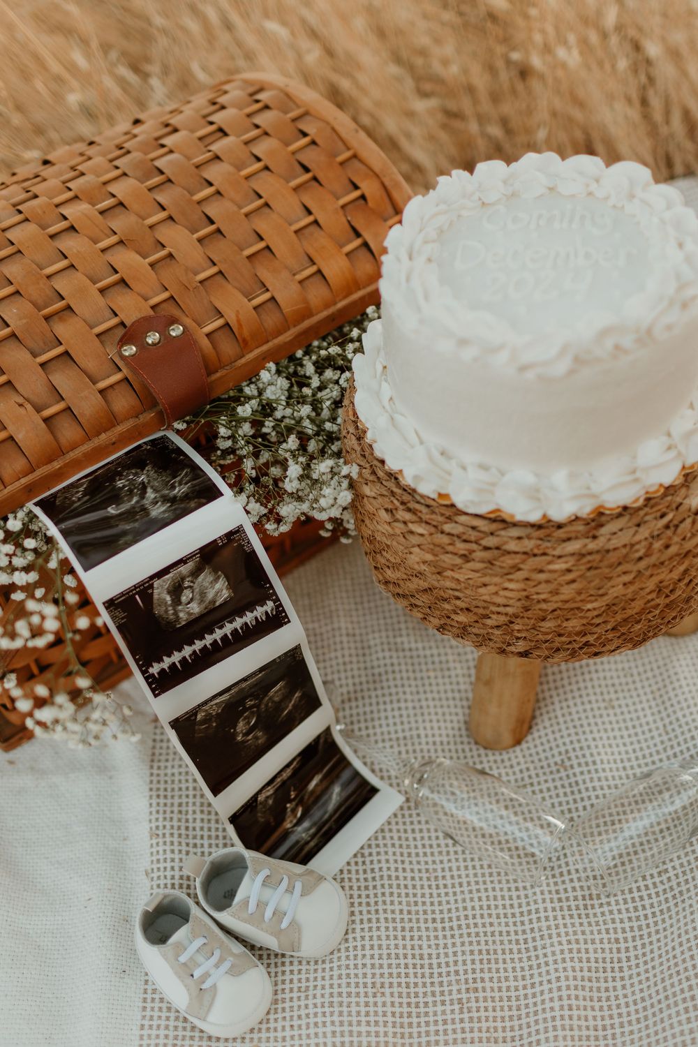 A series of polaroid photos displayed next to a white cake and baby shoes on a woven basket background.
