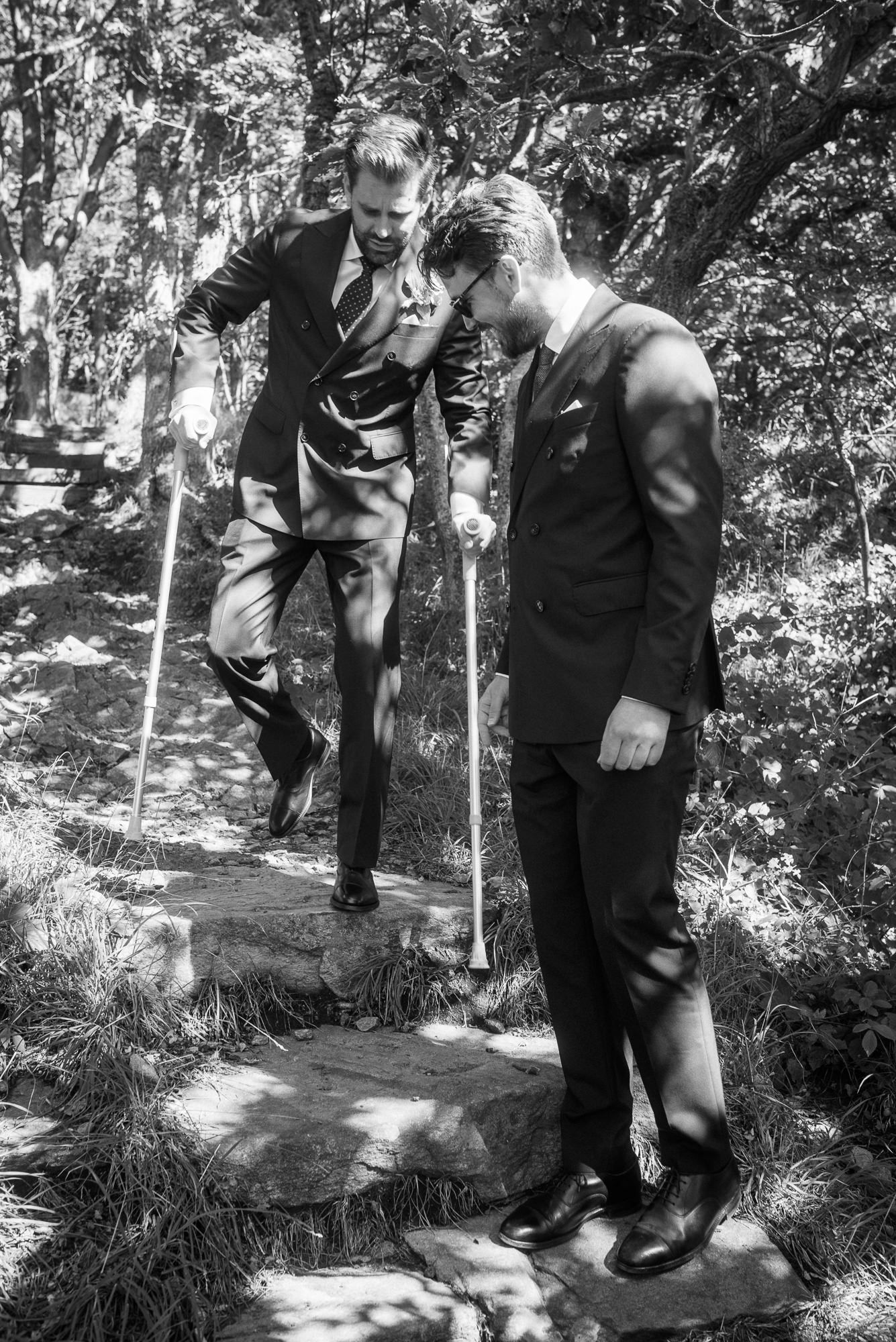 Black and white photo series showing a couple in formal attire walking together along a garden path in dappled sunlight.