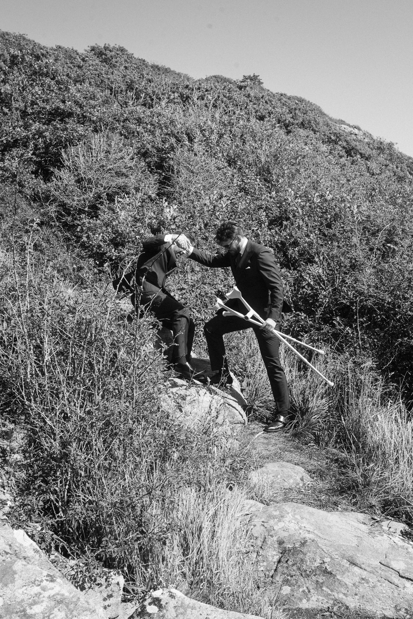 A sequence of black and white photos showing a person climbing up a steep rocky hillside with vegetation.