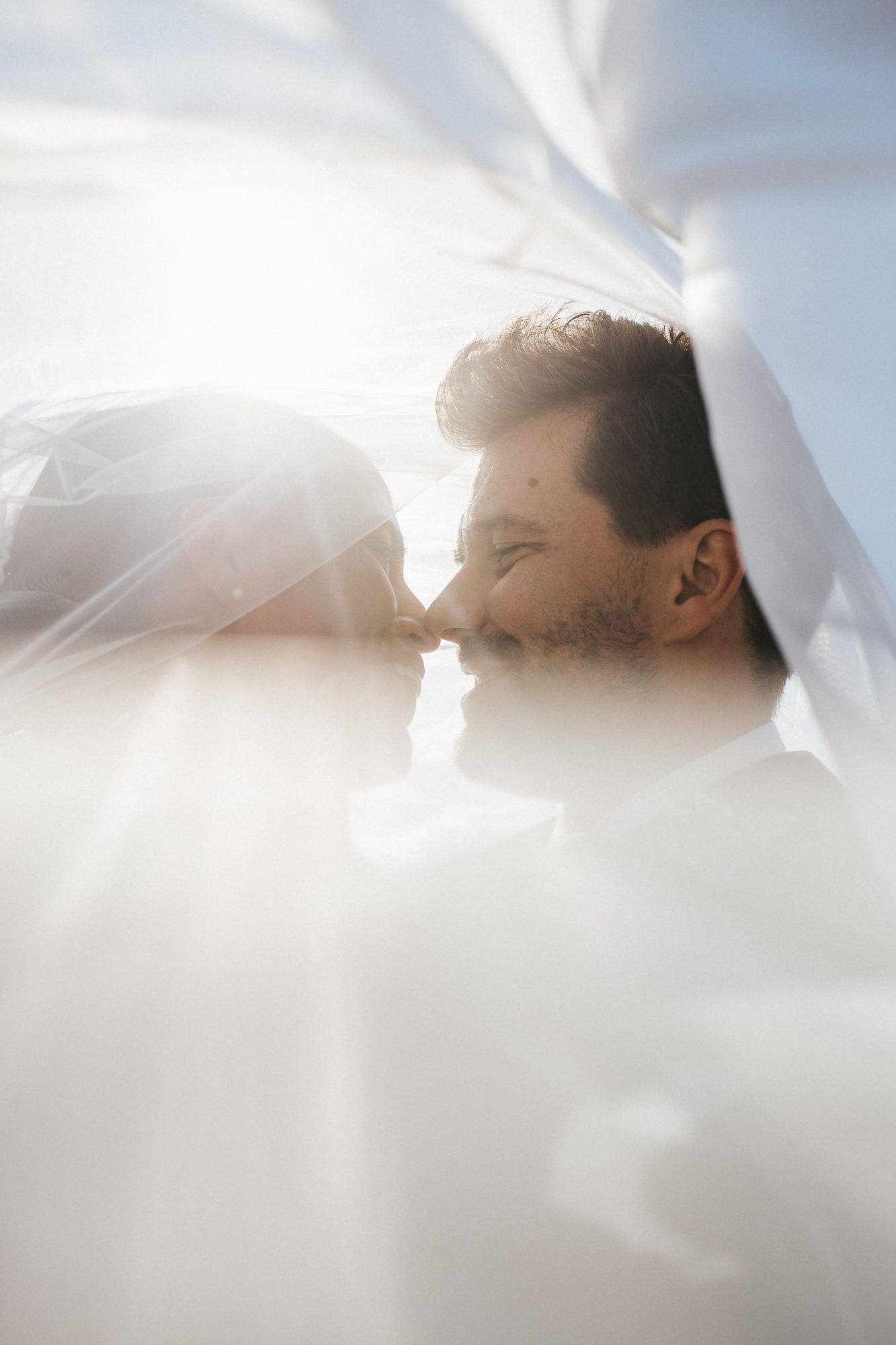 A romantic wedding moment captured through flowing white veil creating a dreamy, ethereal effect.