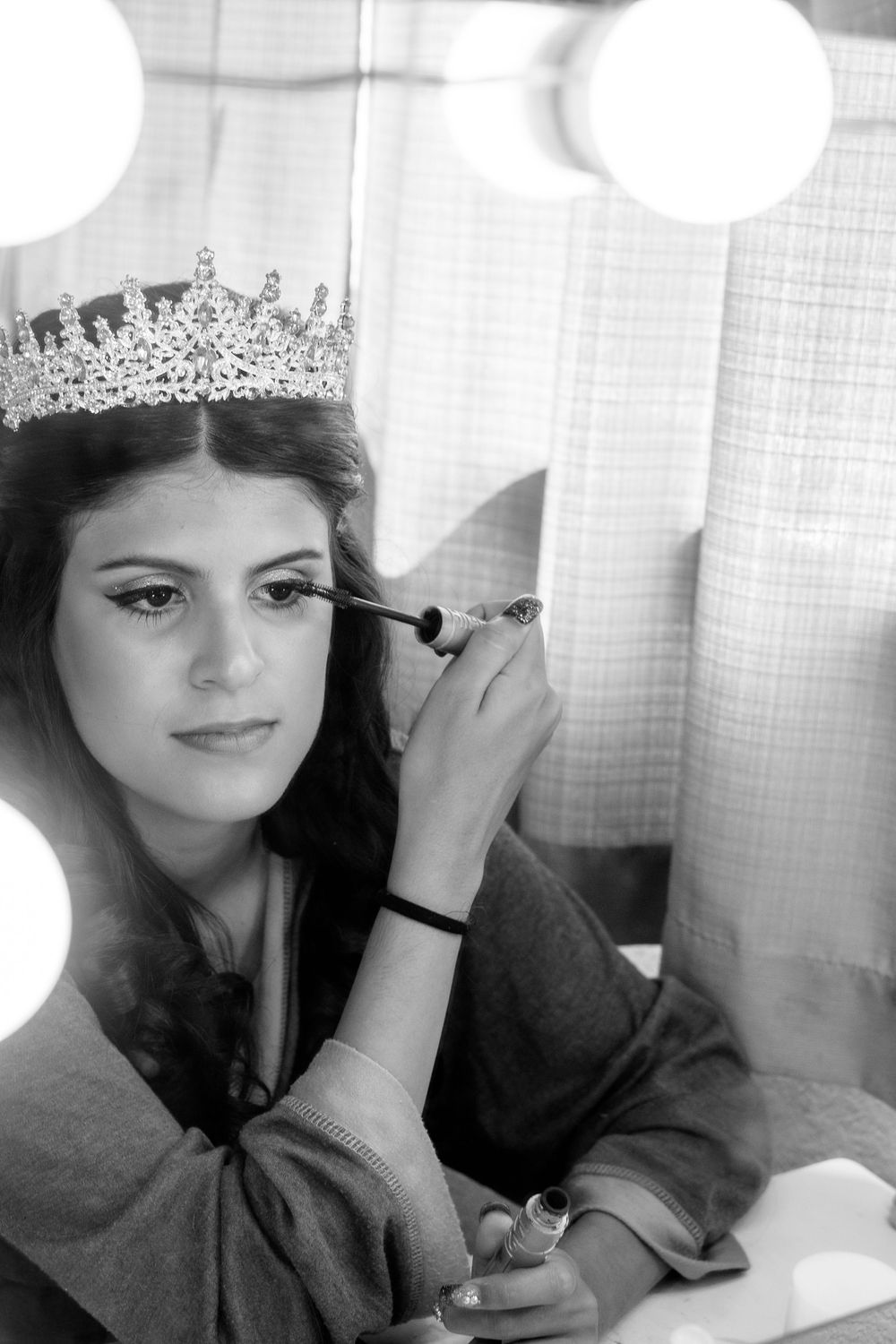 A black and white photo series showing someone wearing a crown and applying makeup in four sequential shots.
