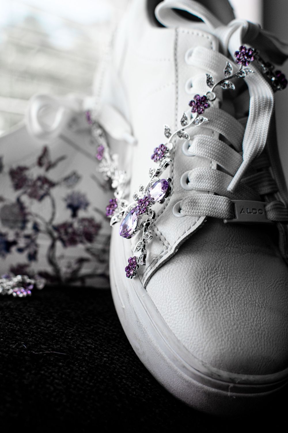 White sneakers with delicate purple floral embroidery details shown in an artistic black and white photo series.