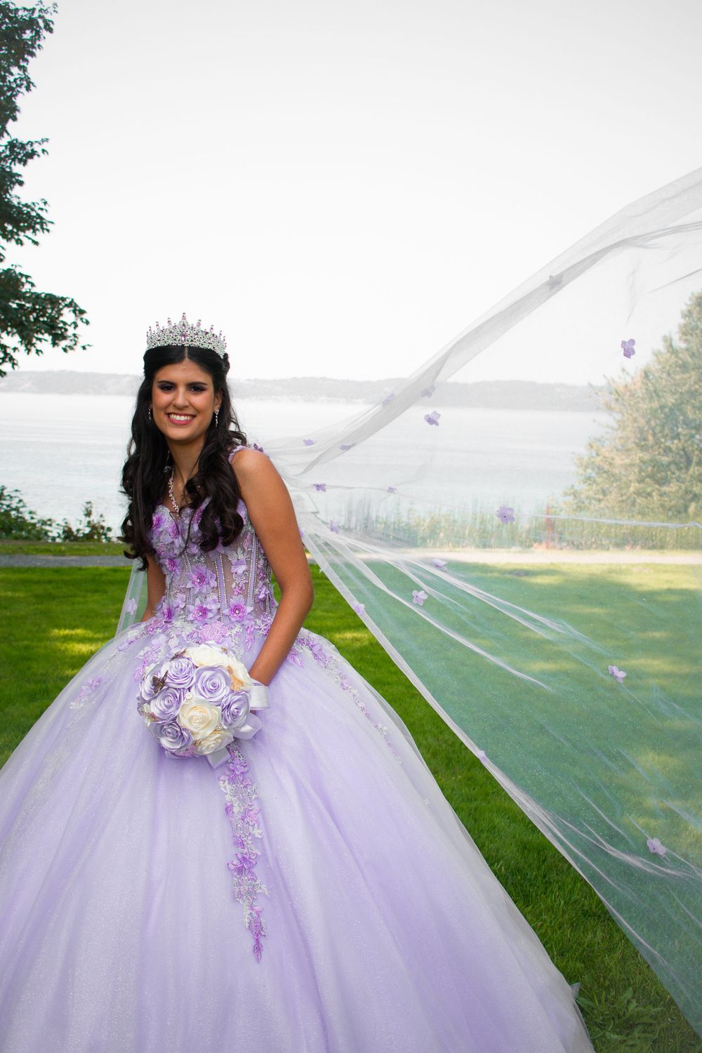 A quinceañera dress in lavender with floral appliques and a flowing tulle skirt creates a dreamy outdoor portrait scene.