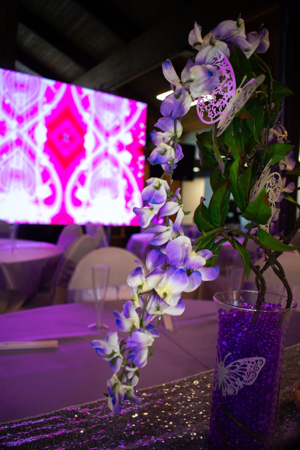 Purple orchids arranged in a vase with a glowing pink geometric backdrop creating an elegant event atmosphere.