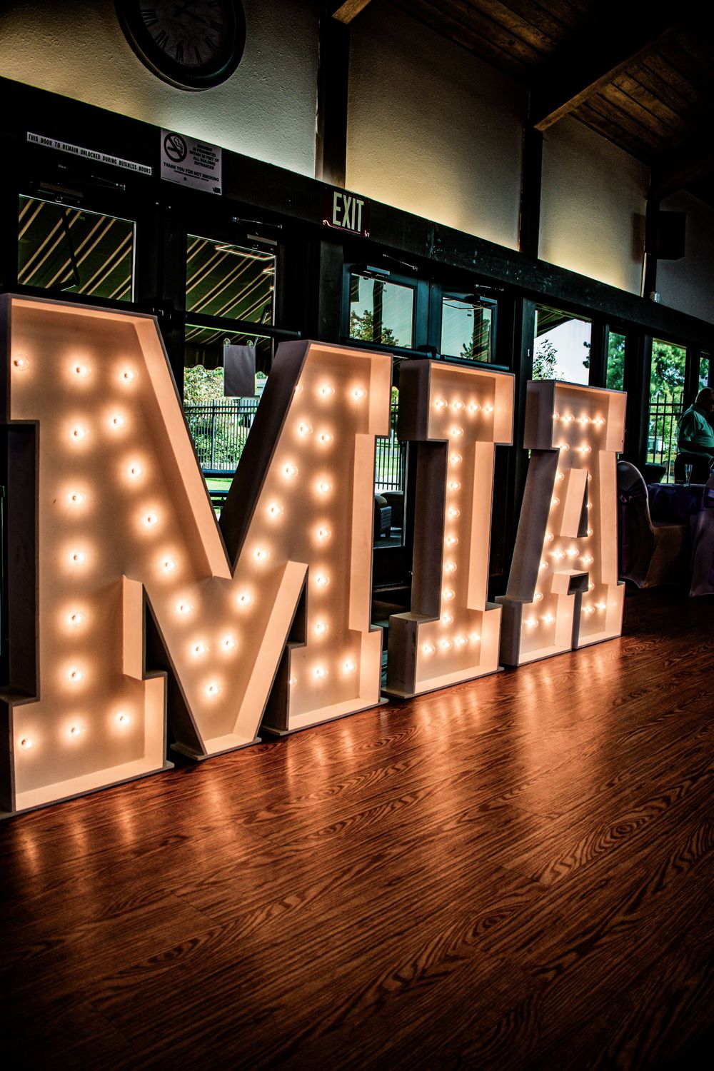 Large illuminated marquee letters spelling MIA on a wooden floor in warm lighting.