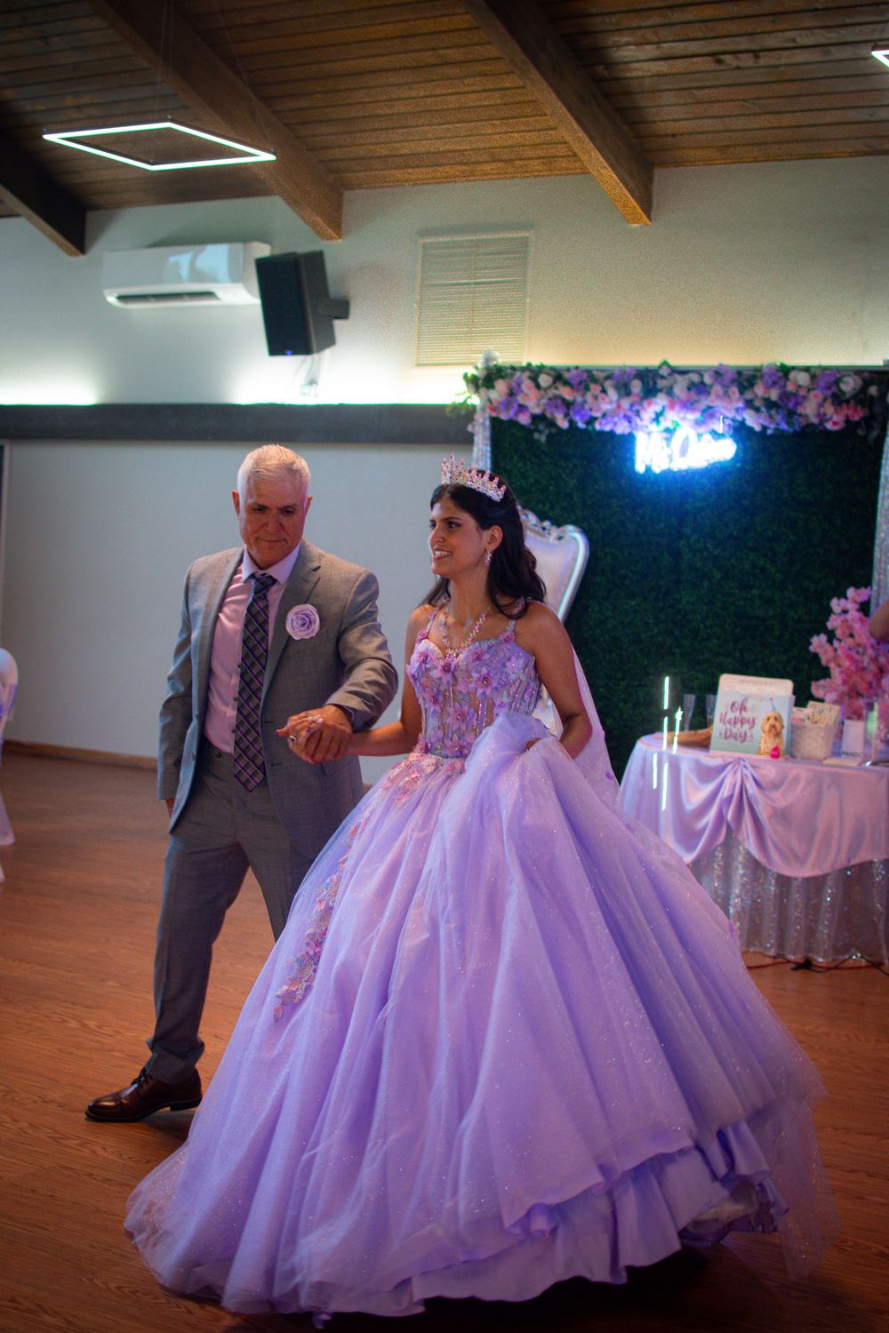 A celebration in a wood-paneled room with a lavender ball gown and floral decorations.