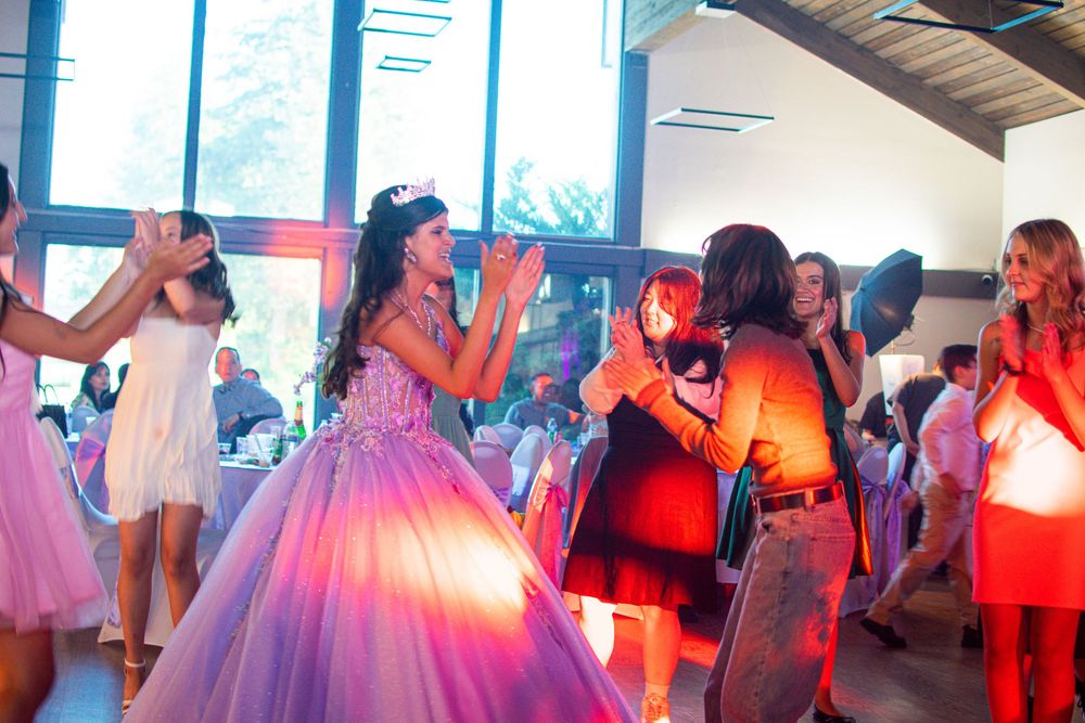 Partygoers dancing and celebrating at a quinceañera or prom with colorful lighting and formal attire.