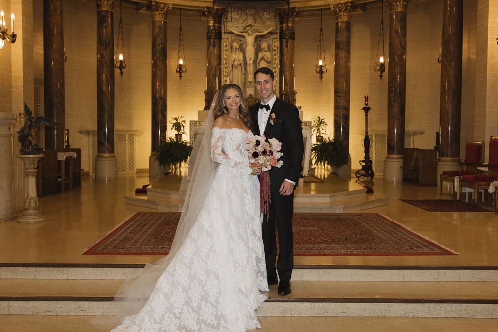 A couple stands at the altar in an ornate church sanctuary with golden walls and glowing candles during their wedding ceremony.