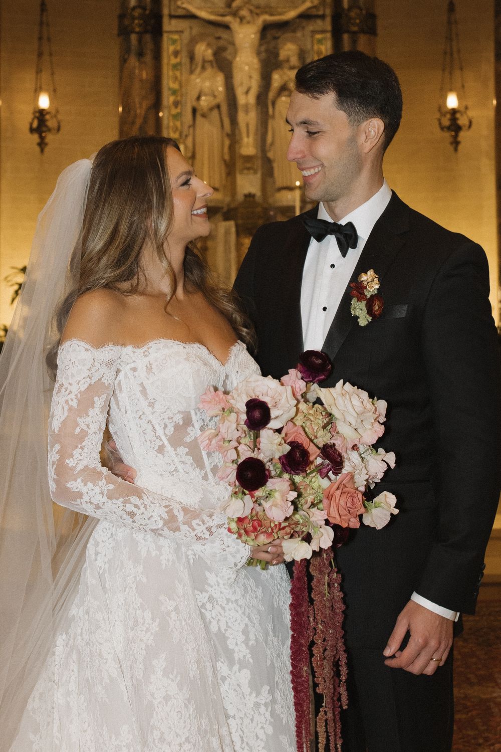 Elegant wedding couple shares romantic moments in formal attire with pink and burgundy floral bouquet.