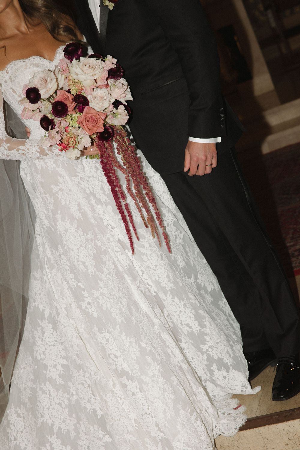 Close-up of a bride's elegant white lace wedding dress with cascading pink and burgundy floral bouquet.