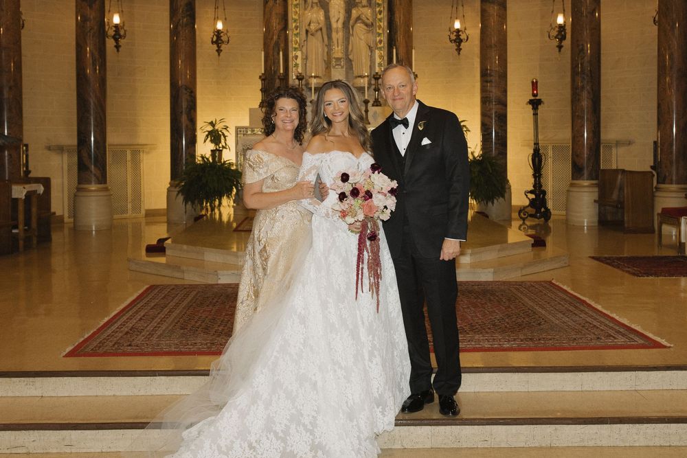 Three people in formal attire stand at the altar of an elegant church during a wedding ceremony.