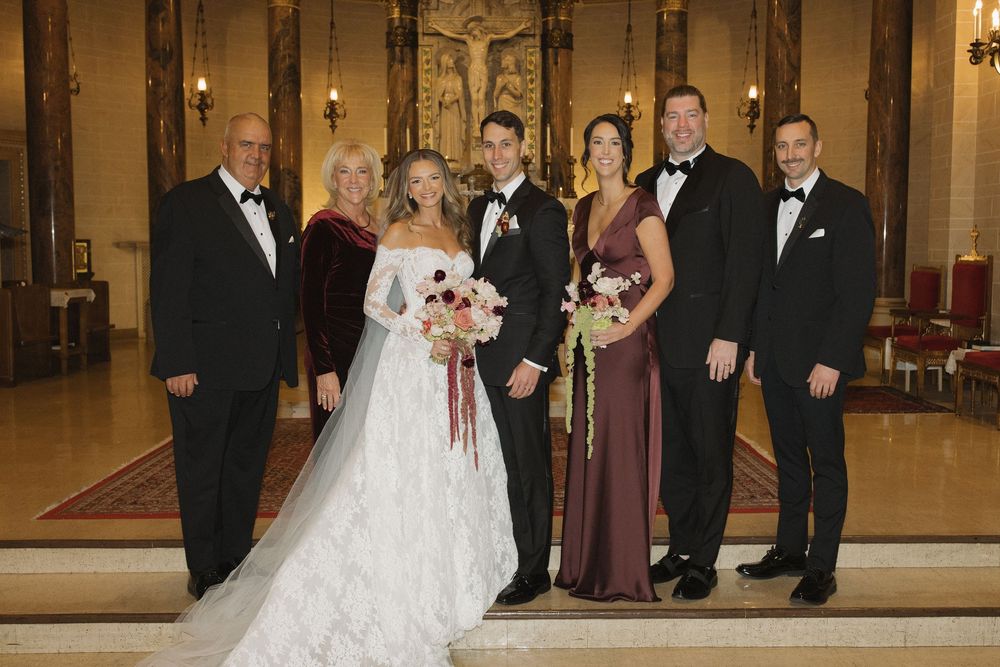 Wedding party members in formal attire pose together in an elegant venue hallway.