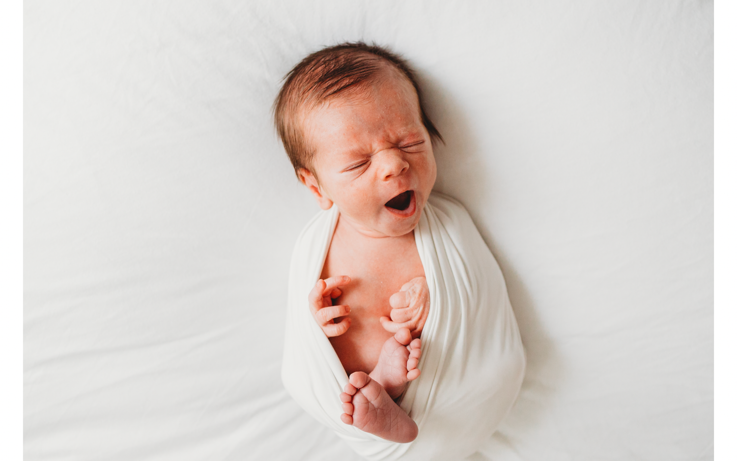 A newborn baby swaddled in white fabric lies on a light background while making different facial expressions.