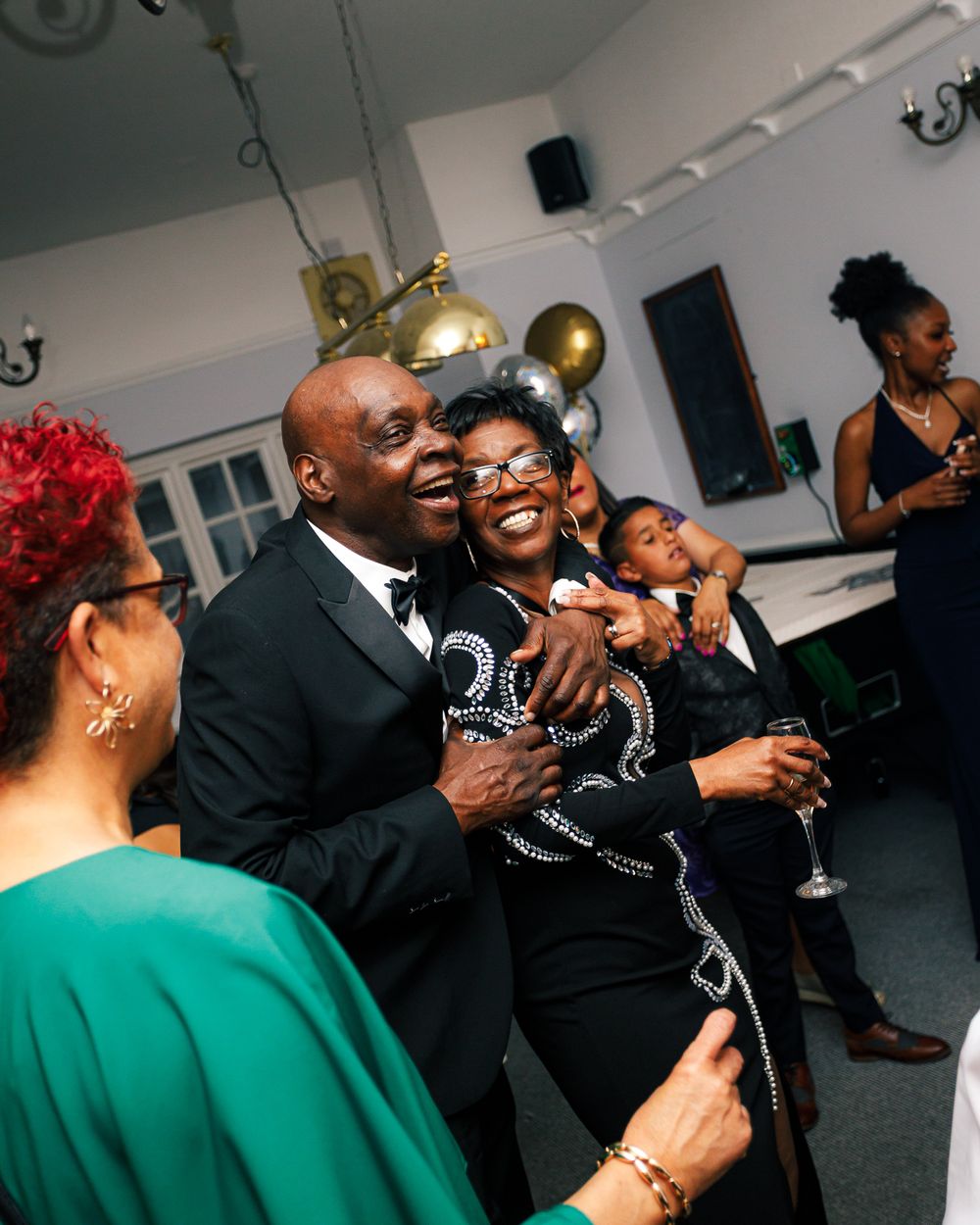 Guests in formal attire enjoying a celebration with drinks and laughter at an indoor event.