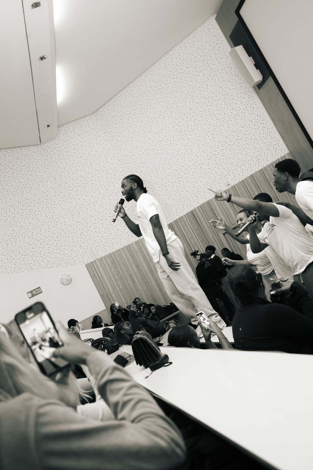Black and white photo of a performer on stage with audience members capturing the moment on their phones.