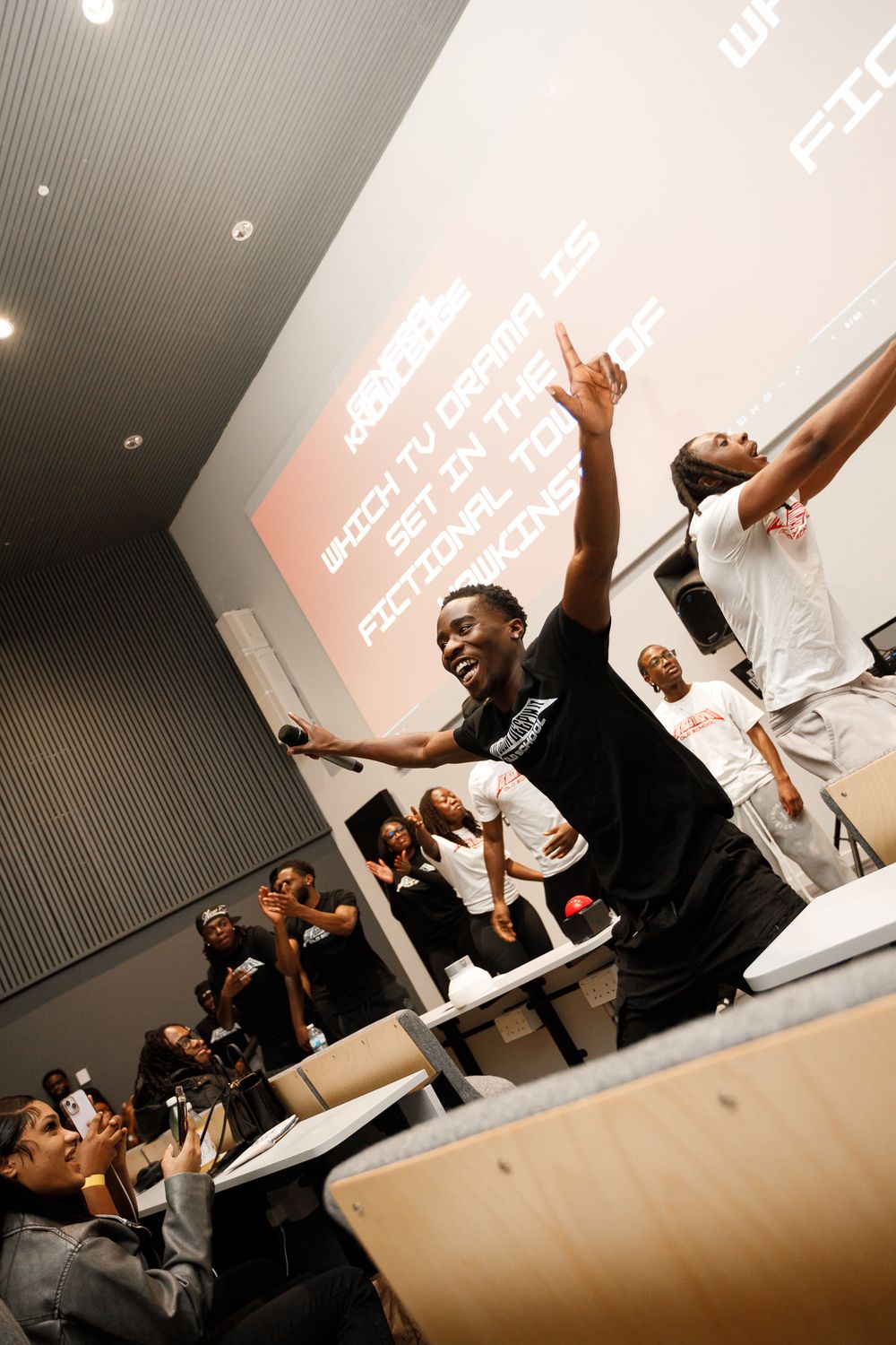A group of people celebrating and cheering enthusiastically in a classroom or meeting room setting.
