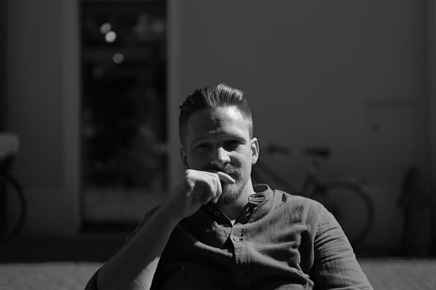 Moody black and white portrait in contemplative pose against dark background.