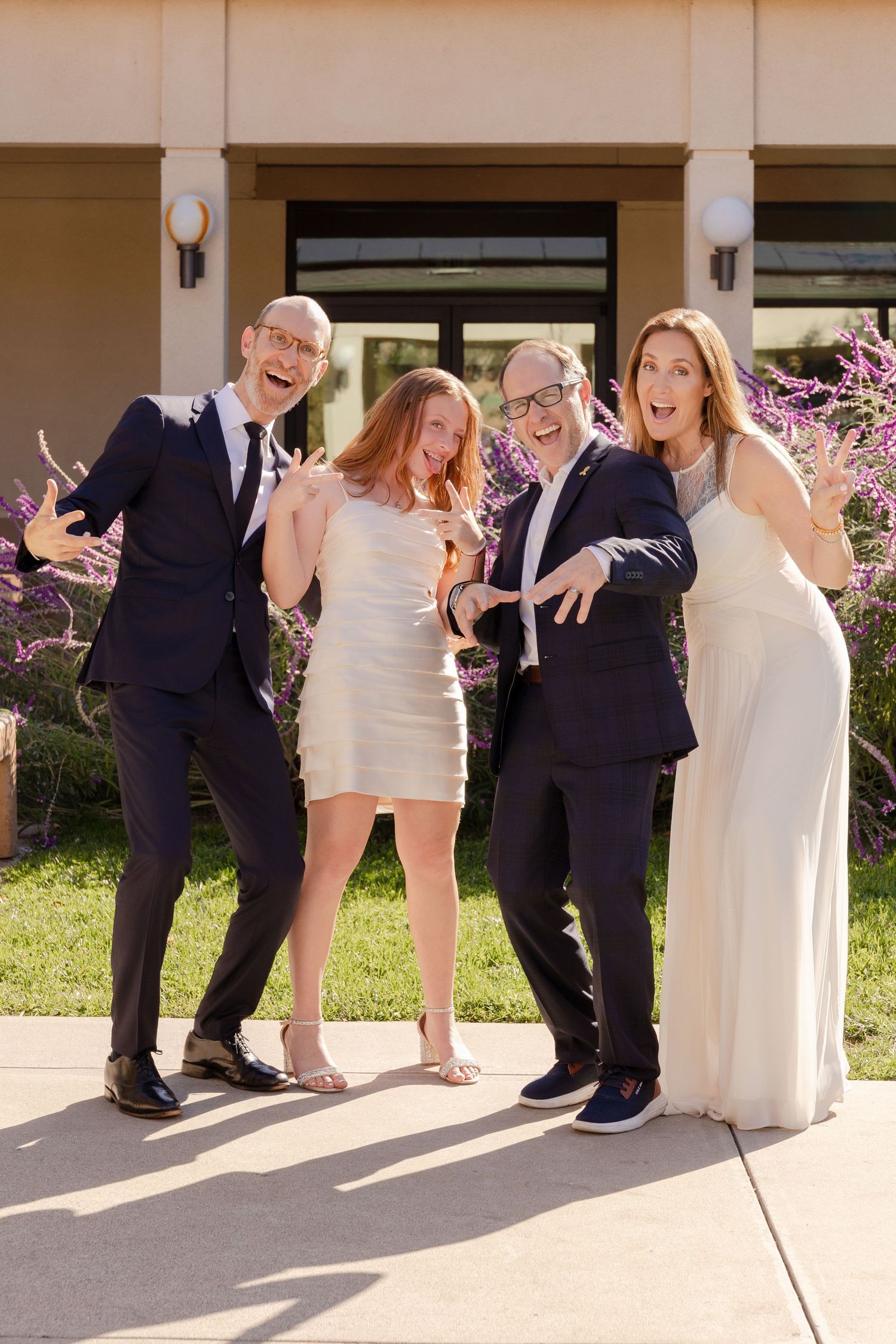 Three people stand together outdoors on a sunny day wearing formal and casual attire.