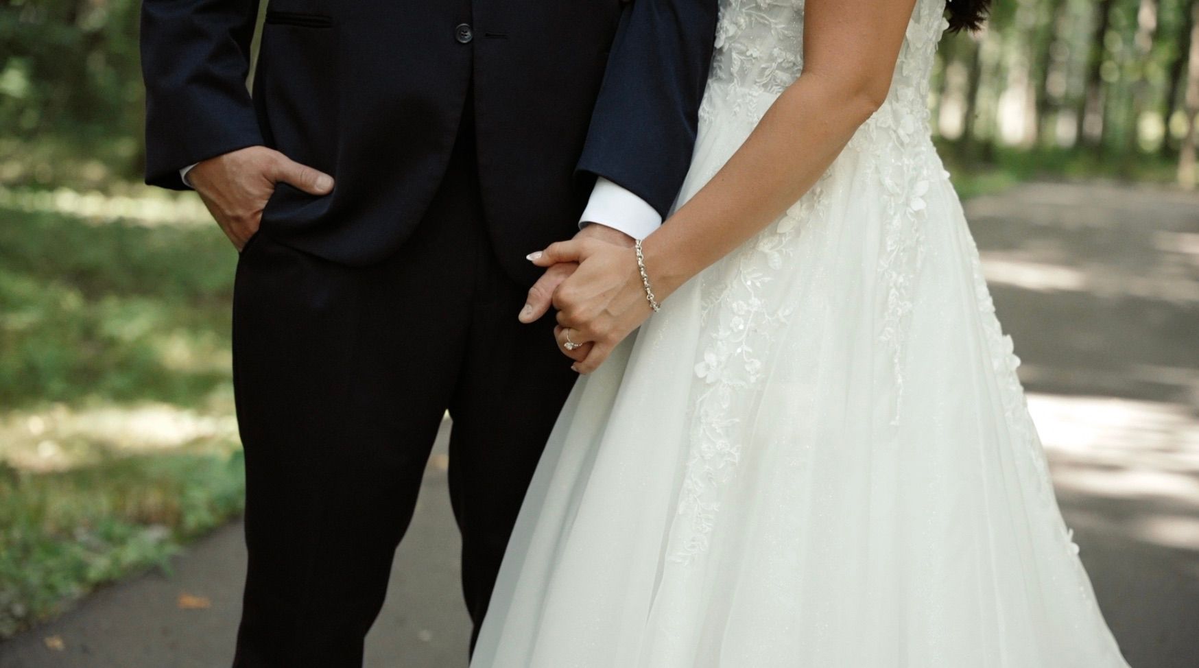 Detail shot of wedding attire showing hands and formal wear against a nature backdrop.