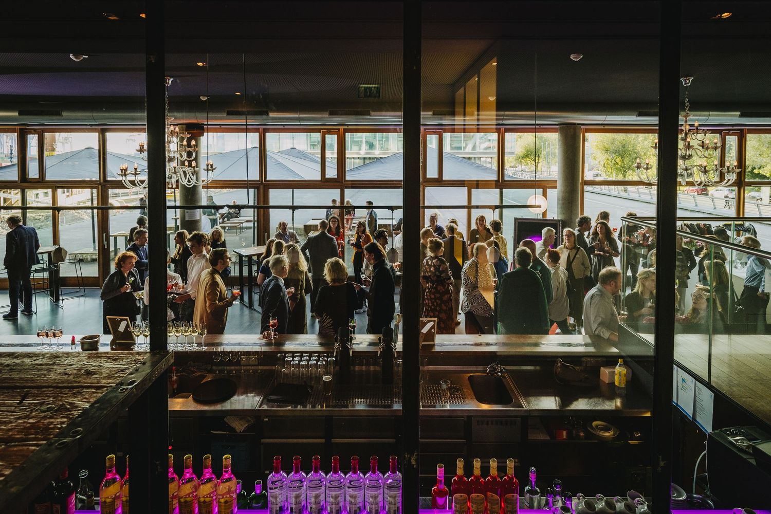 Panoramic view of a crowded modern event venue with large windows and purple accent lighting.
