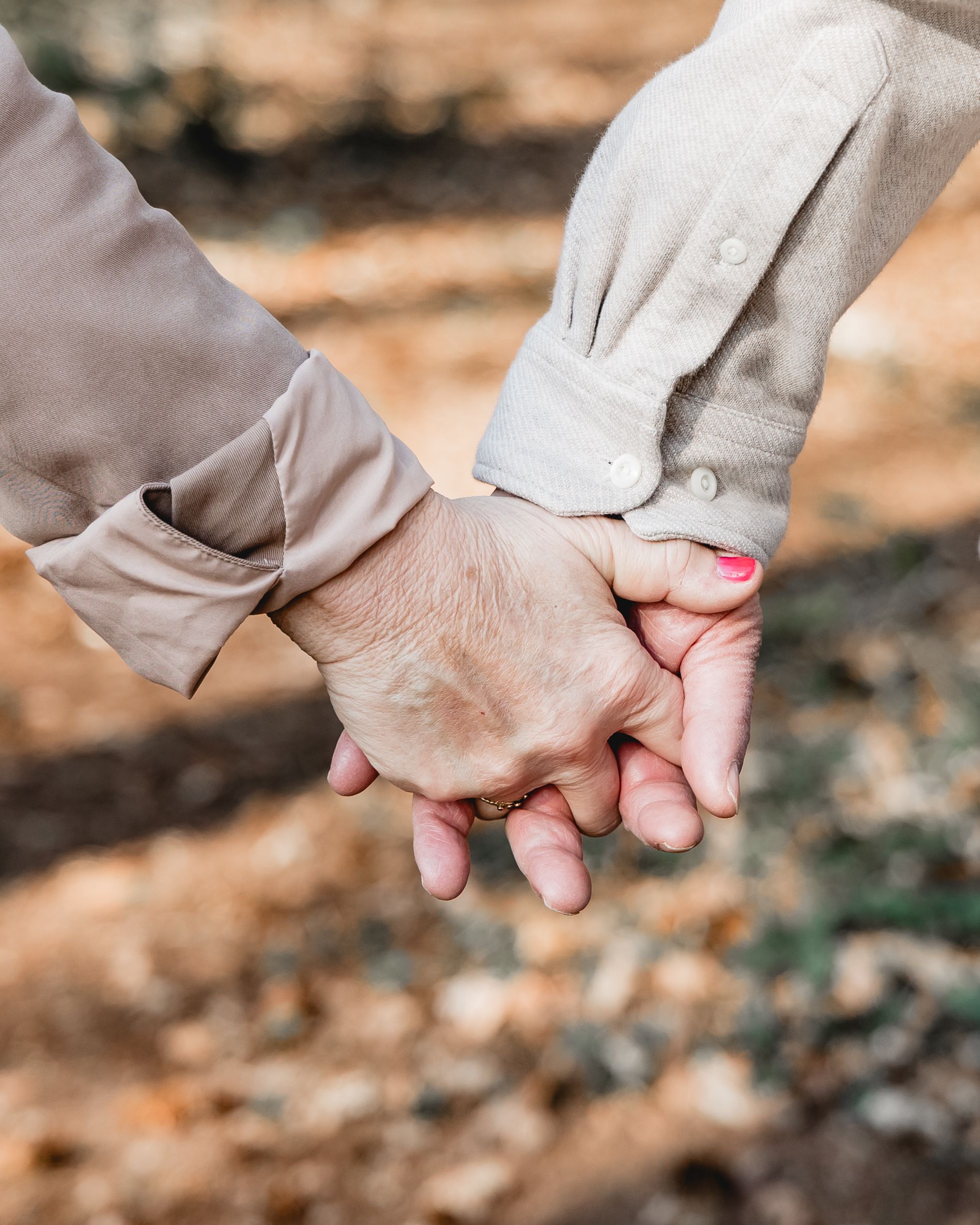Close-up of two hands tenderly holding each other against a blurred natural background.