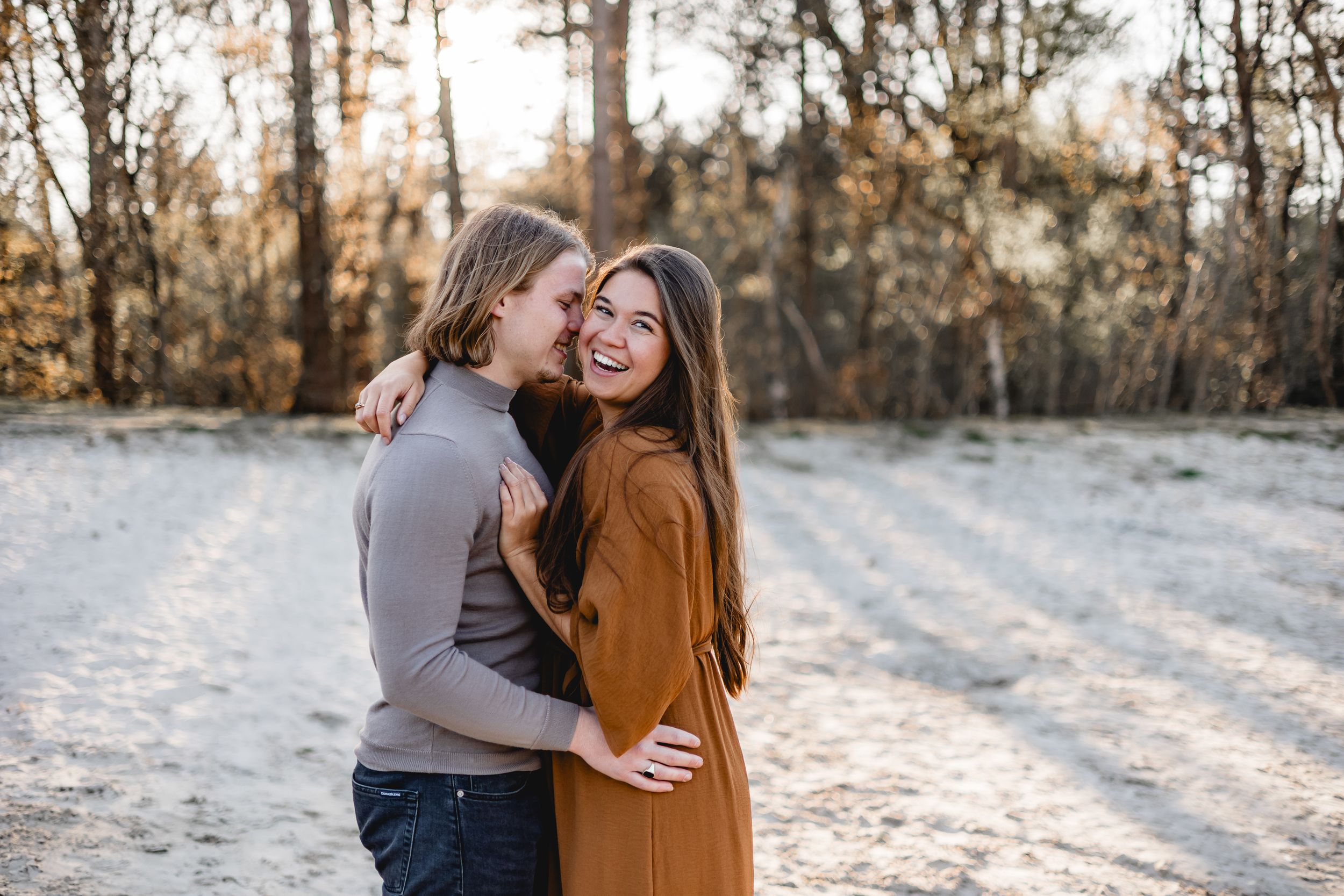 Intimate winter portrait session with golden sunlight streaming through snowy trees.