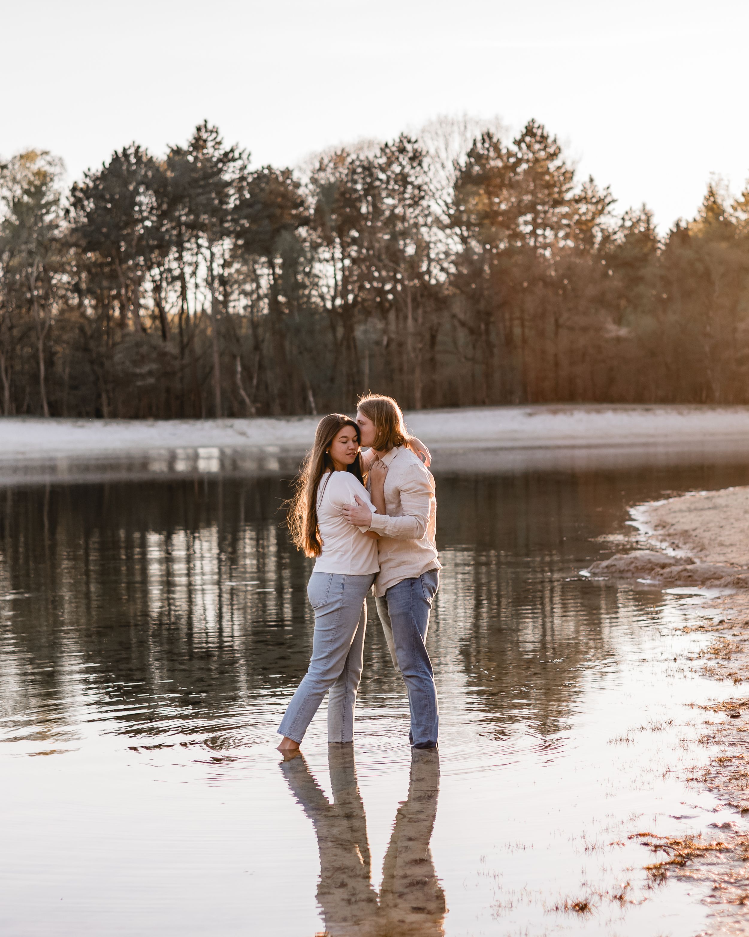 Winter sunset photoshoot by a reflective lake with snow on the shore.