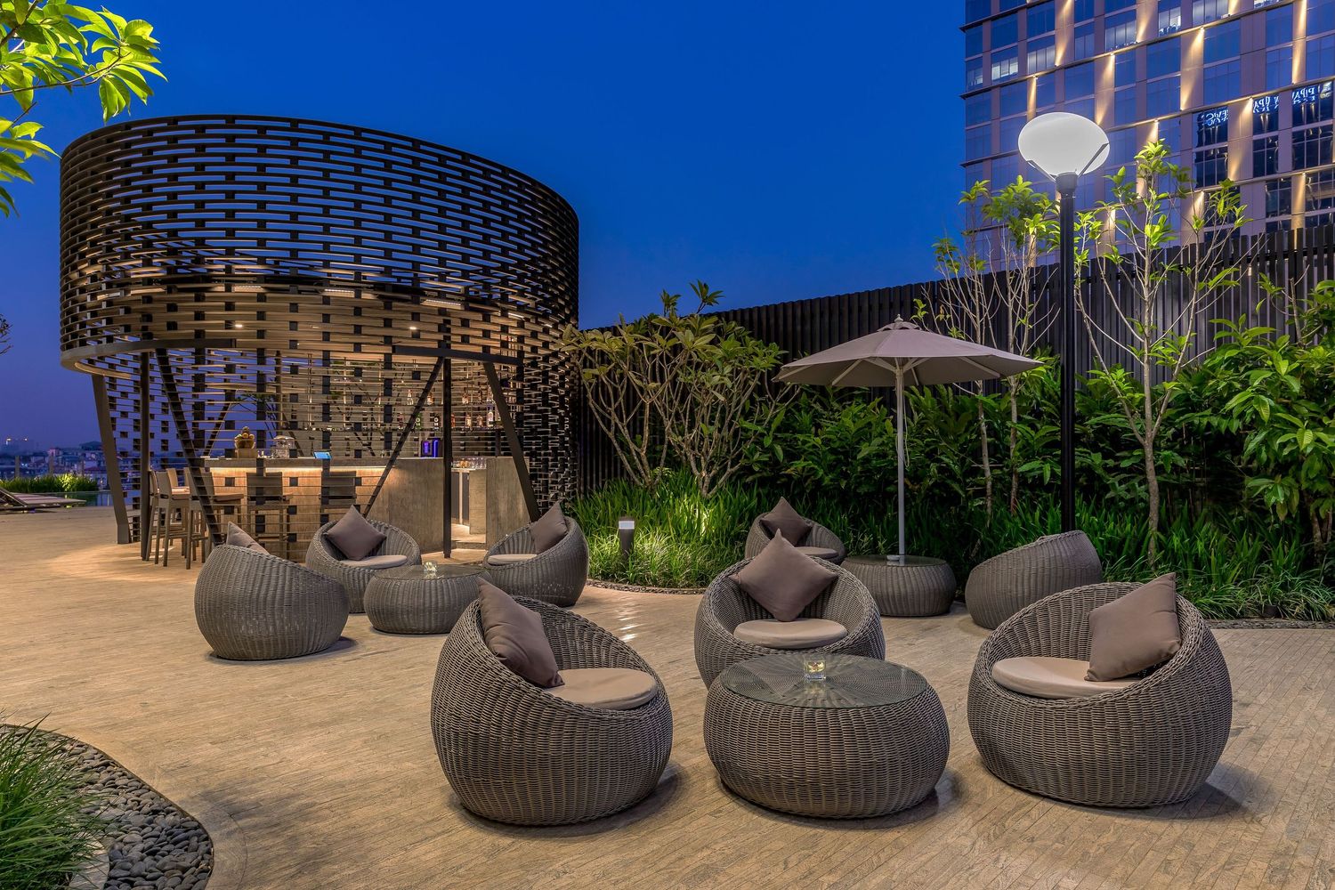 Modern wicker outdoor furniture arranged on a patio with lush greenery and contemporary architectural elements in view.