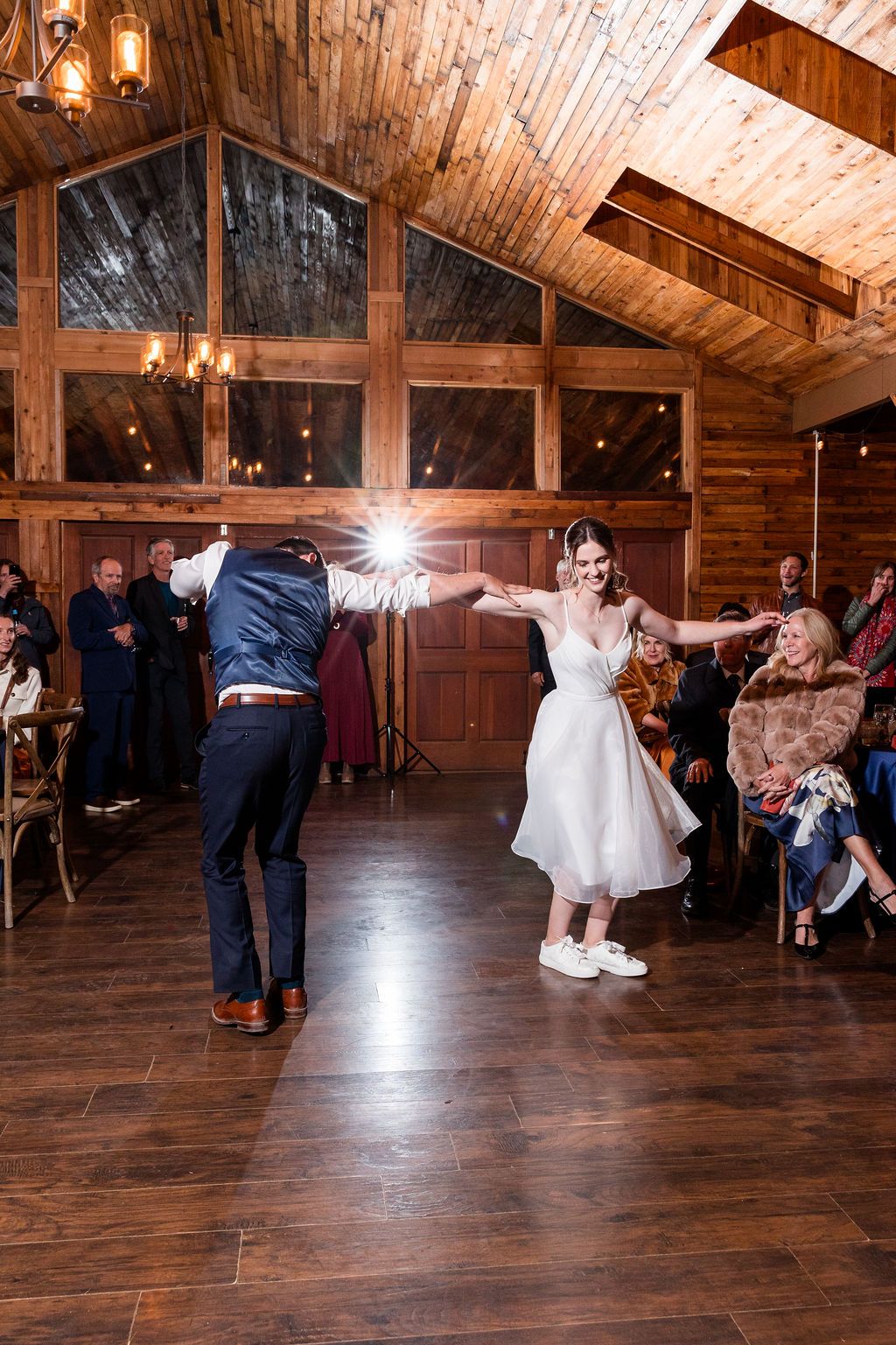 Wedding guests dancing and celebrating on a rustic wooden dance floor in a barn venue with warm lighting.