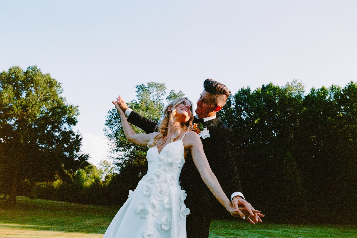 Wedding couple dances together in a romantic outdoor setting at sunset in a grassy field.