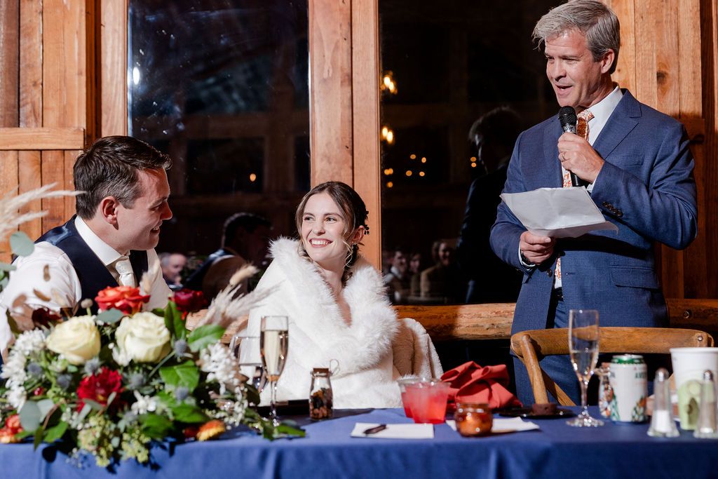Wedding reception guests seated at long tables inside a rustic wooden barn venue during dinner service.
