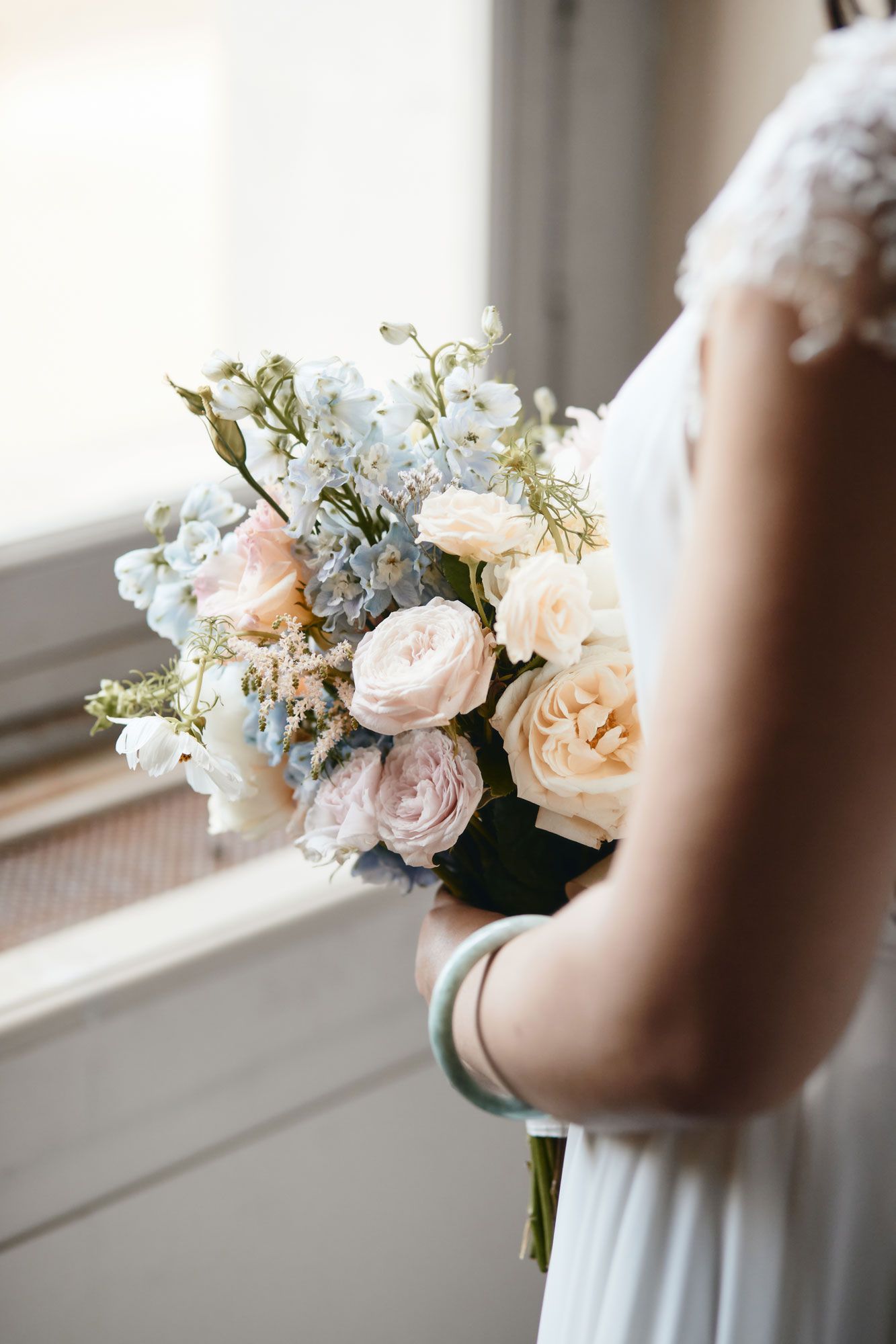 Delicate bridal bouquet featuring pale pink roses and white flowers near a window.