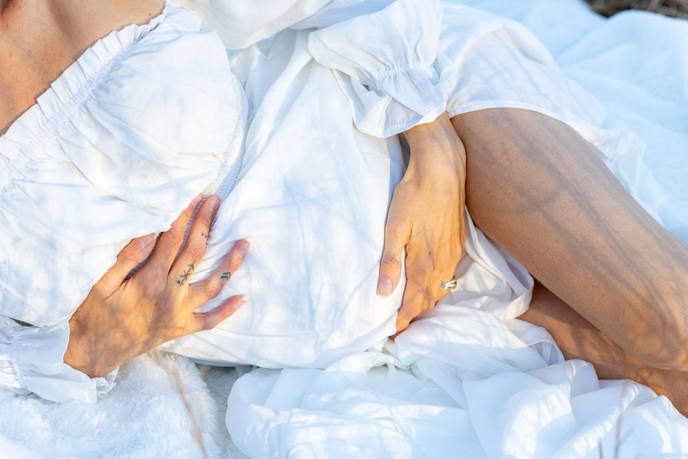A pregnant woman cradles her belly laying in a field on a white blanket in a cinematic maternity photo