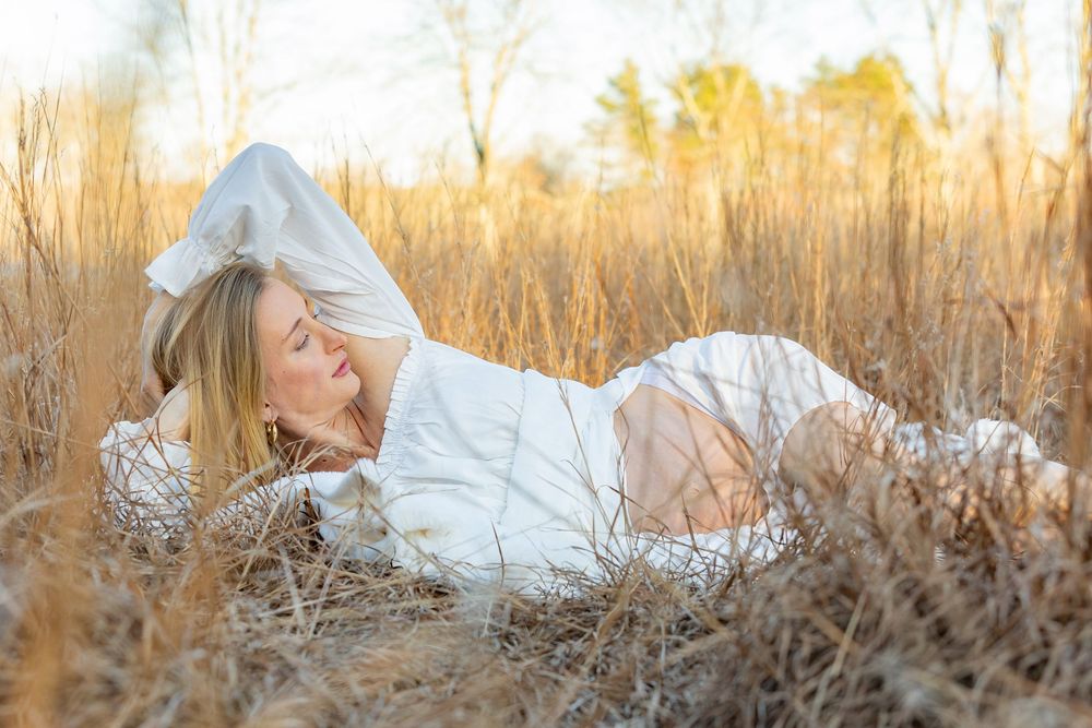 A dreamy outdoor portrait in a golden field at sunset with soft natural lighting and dried winter grasses during a maternity photo session.