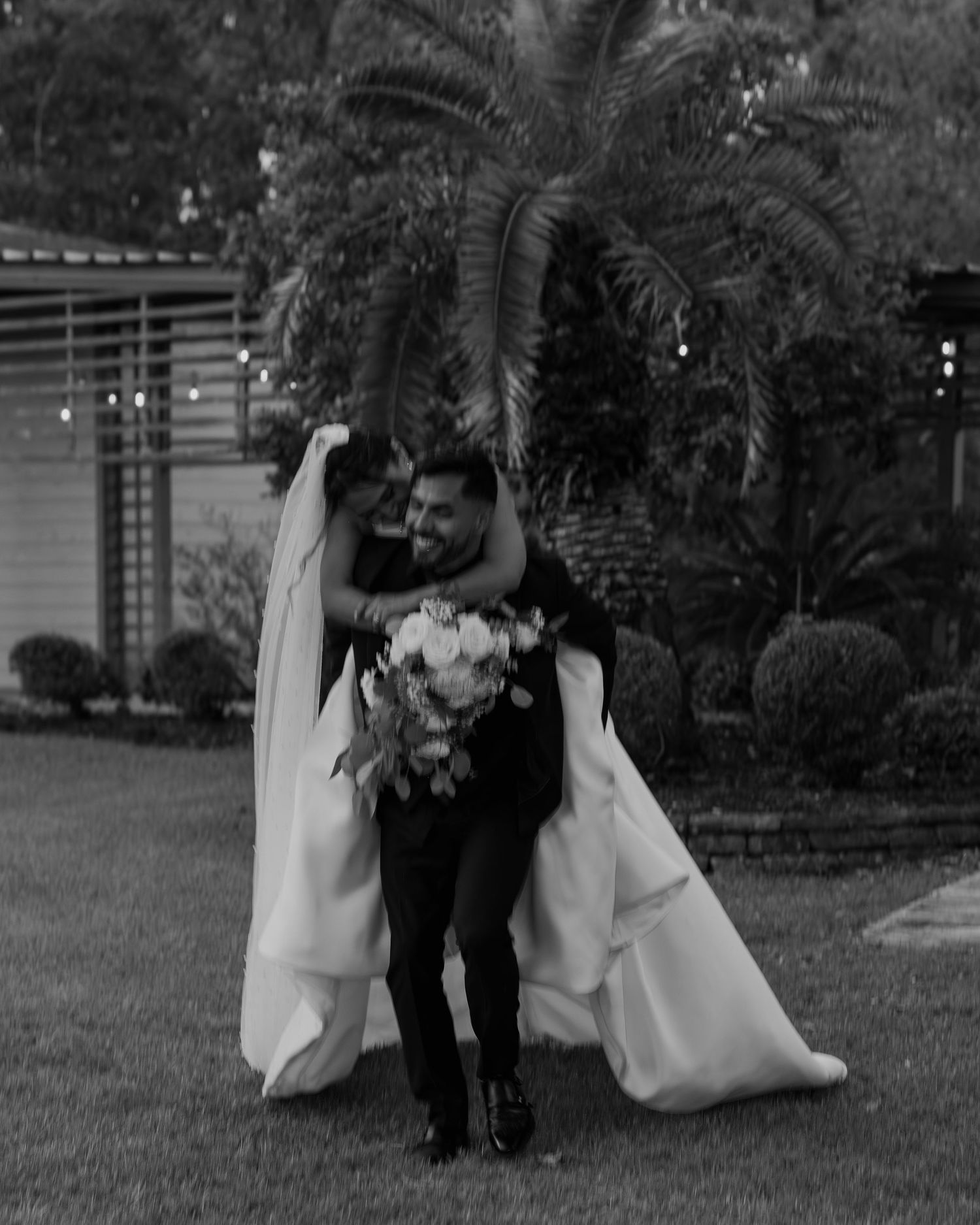 Black and white photo of a couple dancing on grass during their wedding celebration.