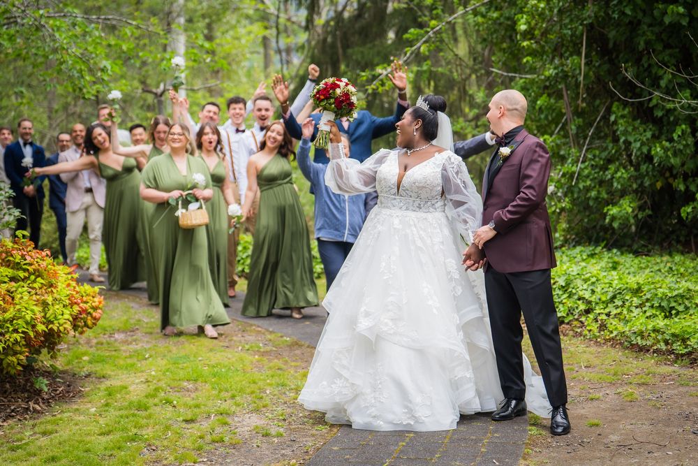 Wedding party walking together on a tree-lined garden path with bridesmaids in sage green dresses.