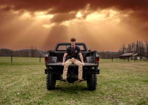 Dramatic panoramic sunset over a grassy field with a pickup truck silhouetted against the orange sky.