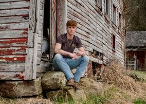 Casual portrait sitting on rock against weathered wooden barn wall.