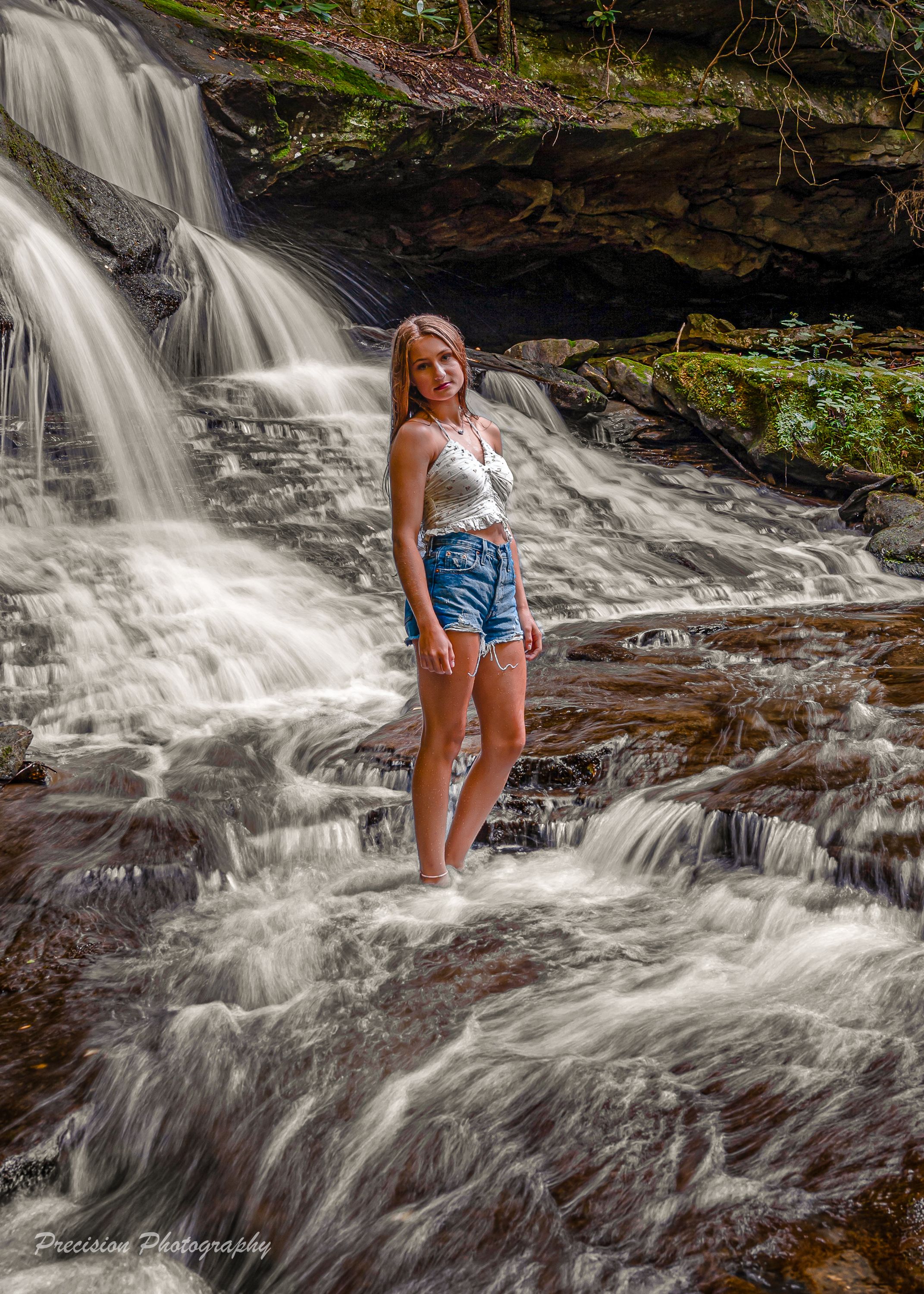 Rushing waterfall cascading over dark rocks with white water spray in a natural forest setting.