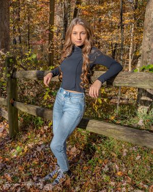 Autumn forest scene with wooden fence and fallen orange leaves along a rustic path.