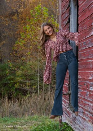 Weathered red barn wall with peeling paint against autumn foliage background.