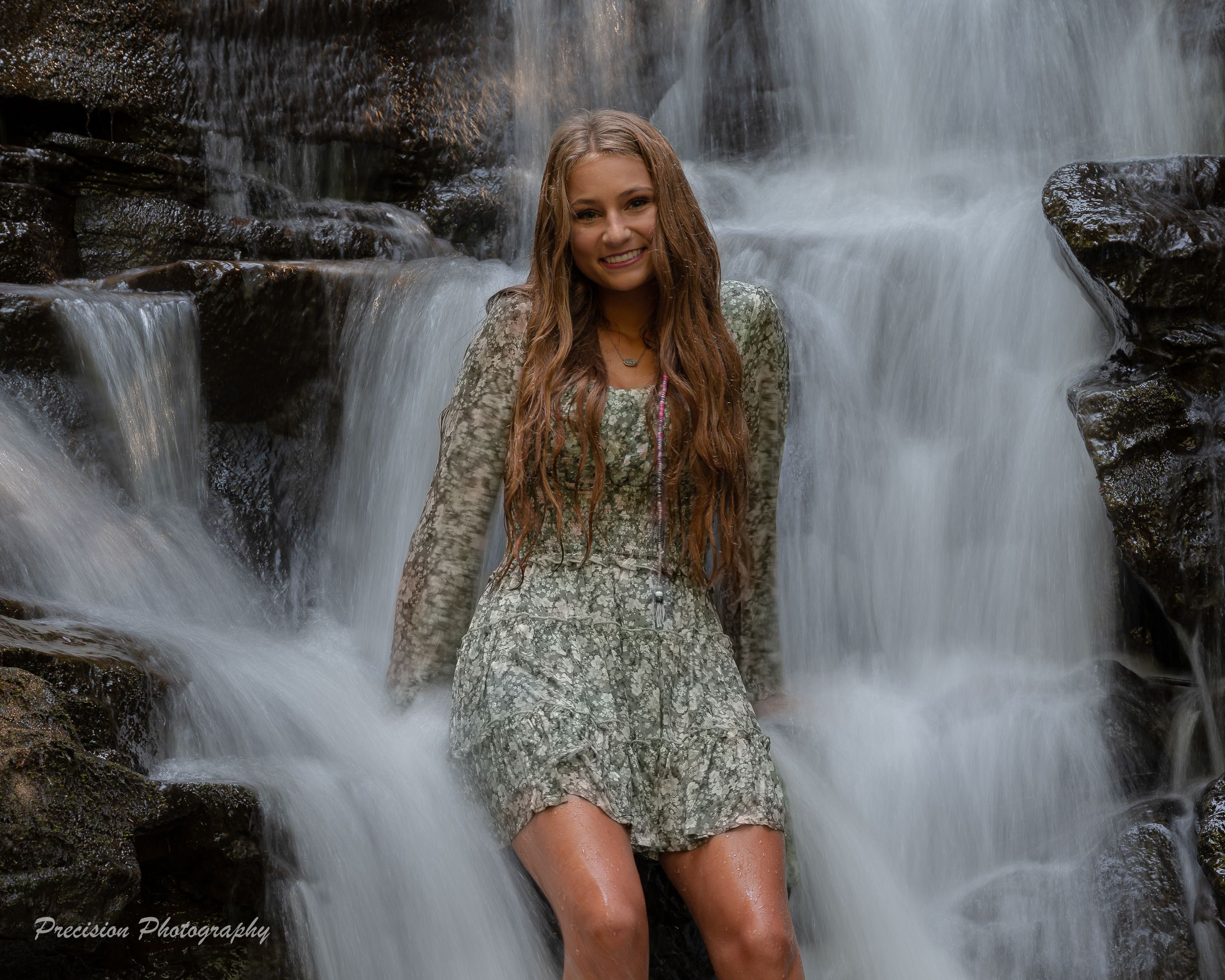 A person poses in a floral dress against a cascading waterfall backdrop creating a dreamy outdoor portrait.