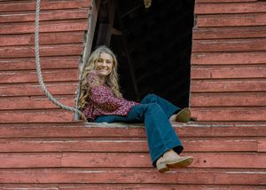 A rustic red barn wall with weathered wooden siding and a dark window opening provides a vintage architectural backdrop.