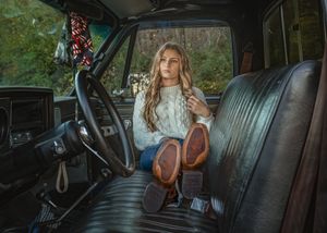 A person sits in a vintage car with blue leather interior and sunlight streaming through the windows.