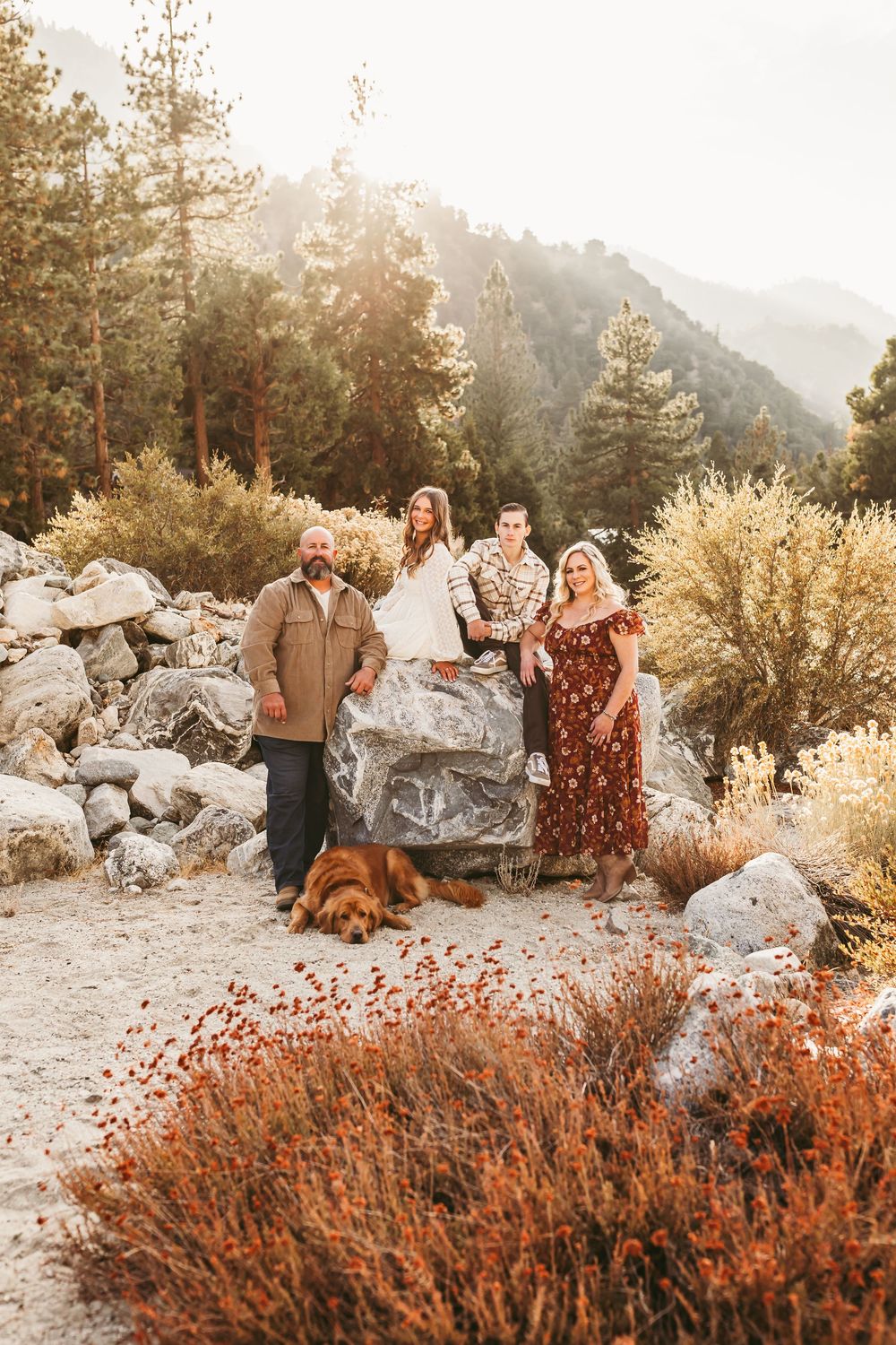 A group poses together on large rocks in a mountainous landscape with golden autumn foliage at sunset.