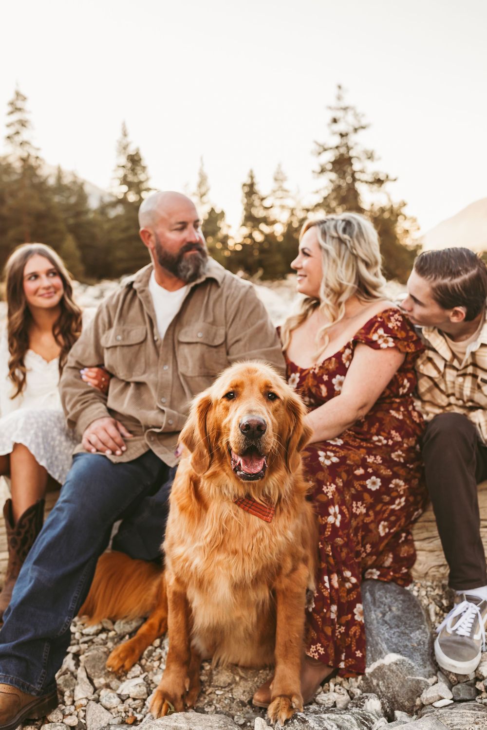 Family group poses casually on rocky terrain with their golden retriever during an outdoor photo session.