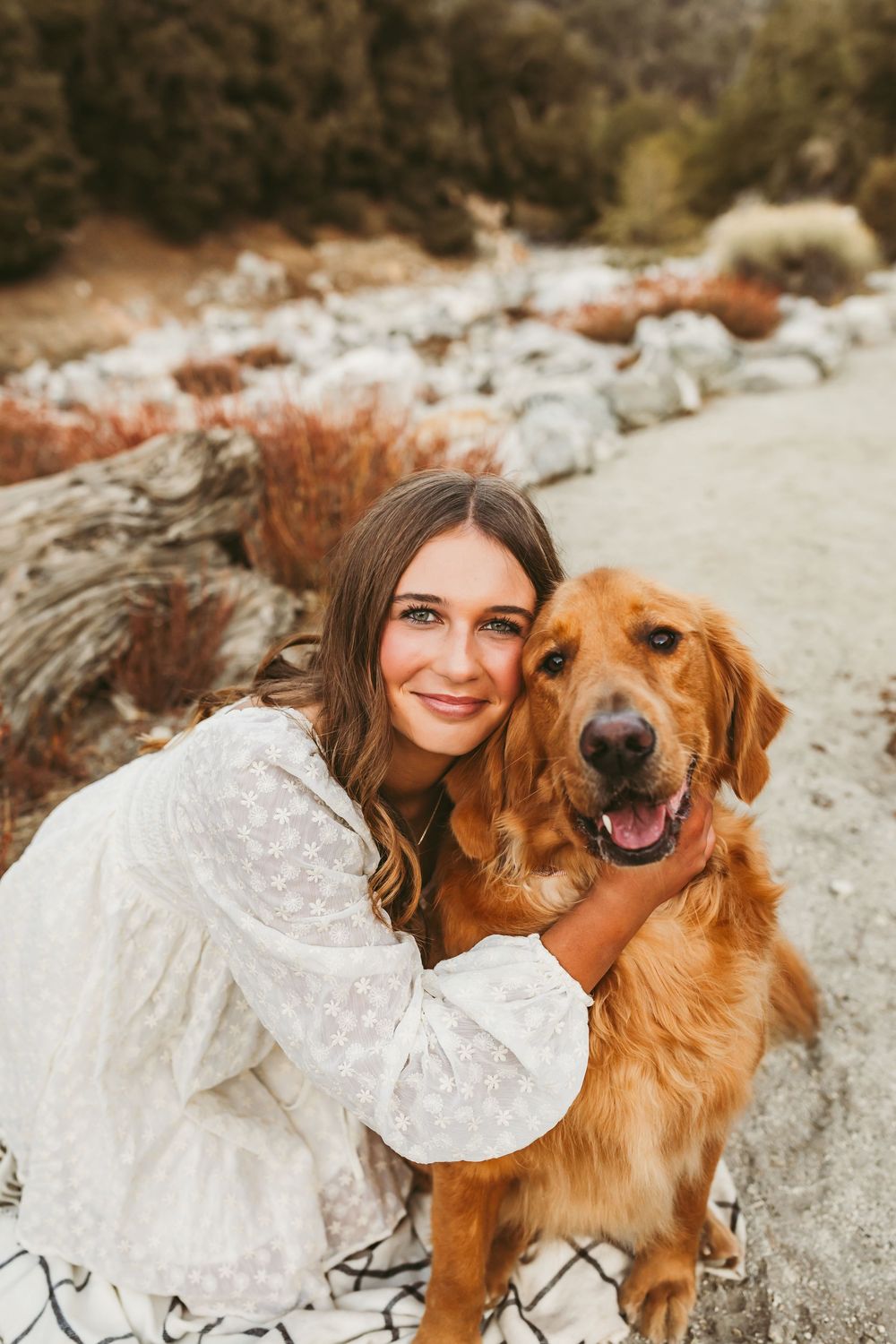 A happy Golden Retriever and someone in a white lace dress pose together on rocky terrain during an outdoor photoshoot.